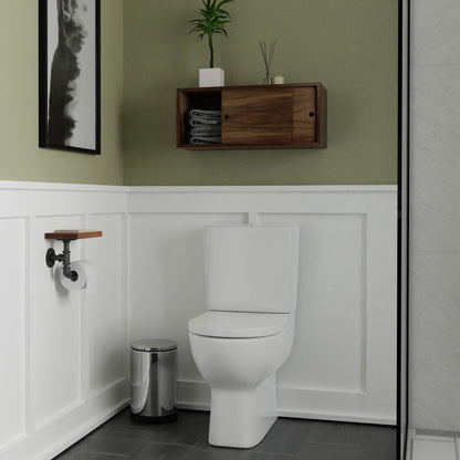 A modern bathroom featuring a white toilet, Krovel Hardwood Floating Storage Cabinet with towels and a plant, metal trash can, toilet paper holder, green upper walls, white wainscoting, and part of the shower on the right.