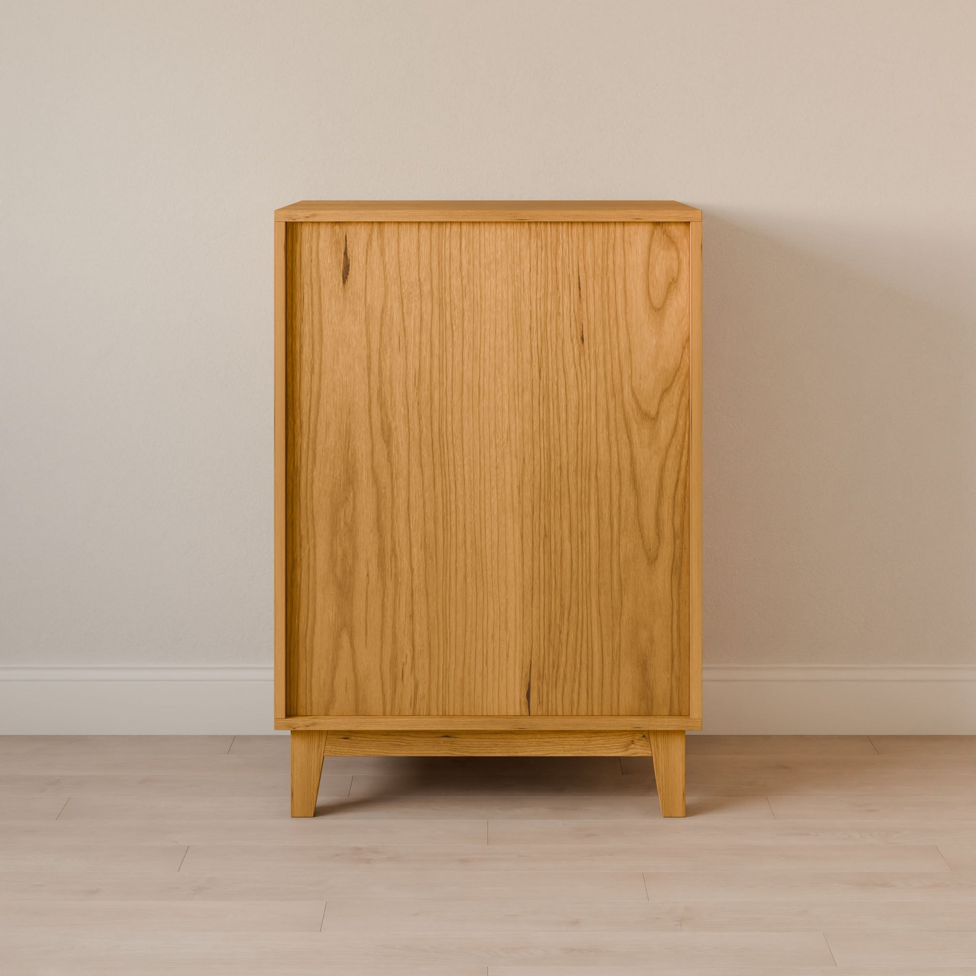 The Krovel Furniture Co. Four Drawer Dresser in Cherry stands on a light wood floor against a pale wall. This premium cabinet, with its minimalist design, clean lines, and natural wood grain patterns, is supported by four tapered legs, showcasing the artistry of sustainable construction.