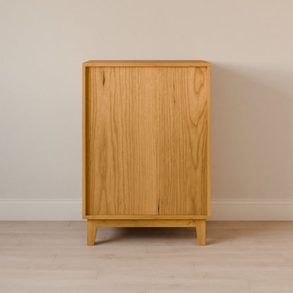 The Krovel Furniture Co. Four Drawer Dresser in Cherry stands on a light wood floor against a pale wall. This premium cabinet, with its minimalist design, clean lines, and natural wood grain patterns, is supported by four tapered legs, showcasing the artistry of sustainable construction.