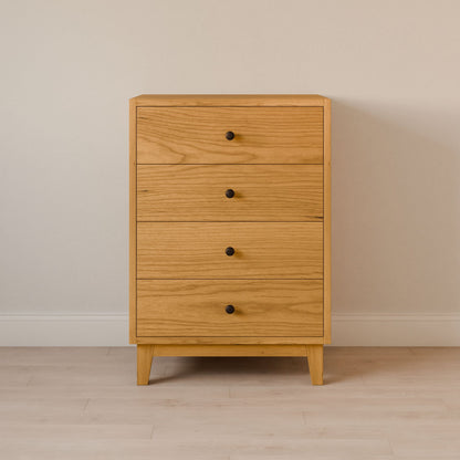The Four Drawer Dresser in Cherry by Krovel Furniture Co. showcases handmade quality with a simple, modern design and clean lines. It features round black knobs and a natural wood finish, perfect for your space against a light wooden floor and beige wall.