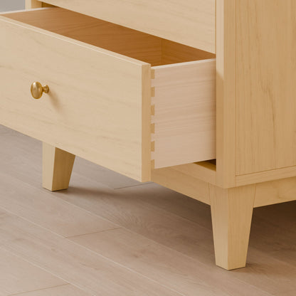 The Krovel Furniture Co. Four Drawer Dresser in Maple, handcrafted with sustainable design, showcases dovetail joints in its open drawer and rests on four angled legs with a round brass-colored knob, elegantly poised on a wooden floor.
