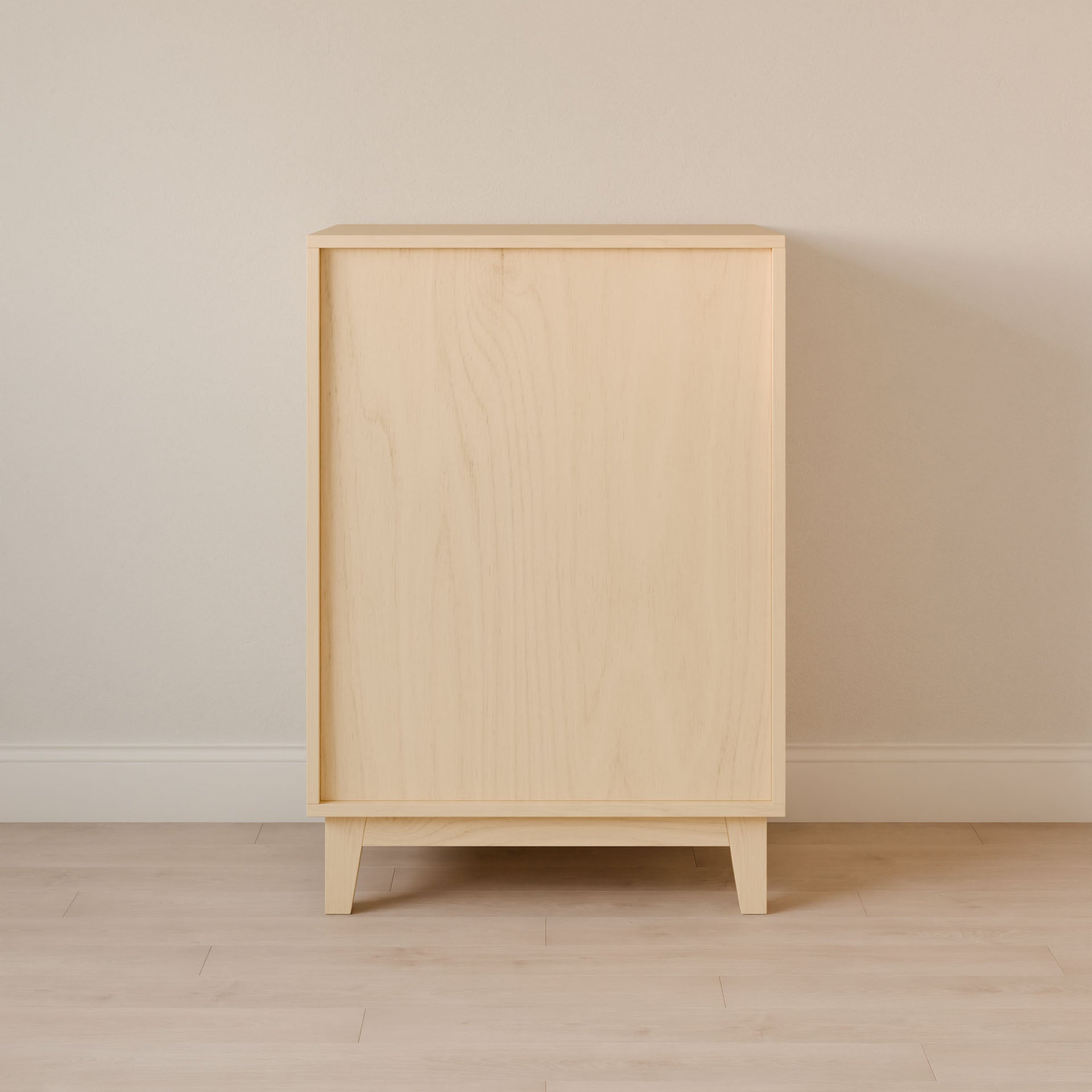 The Four Drawer Dresser in Maple from Krovel Furniture Co. stands against a beige wall, showcasing its minimalist design, tapered legs, and smooth texture. Crafted with sustainable techniques, this premium dressers light finish complements the light-colored floor, highlighting its clean lines.