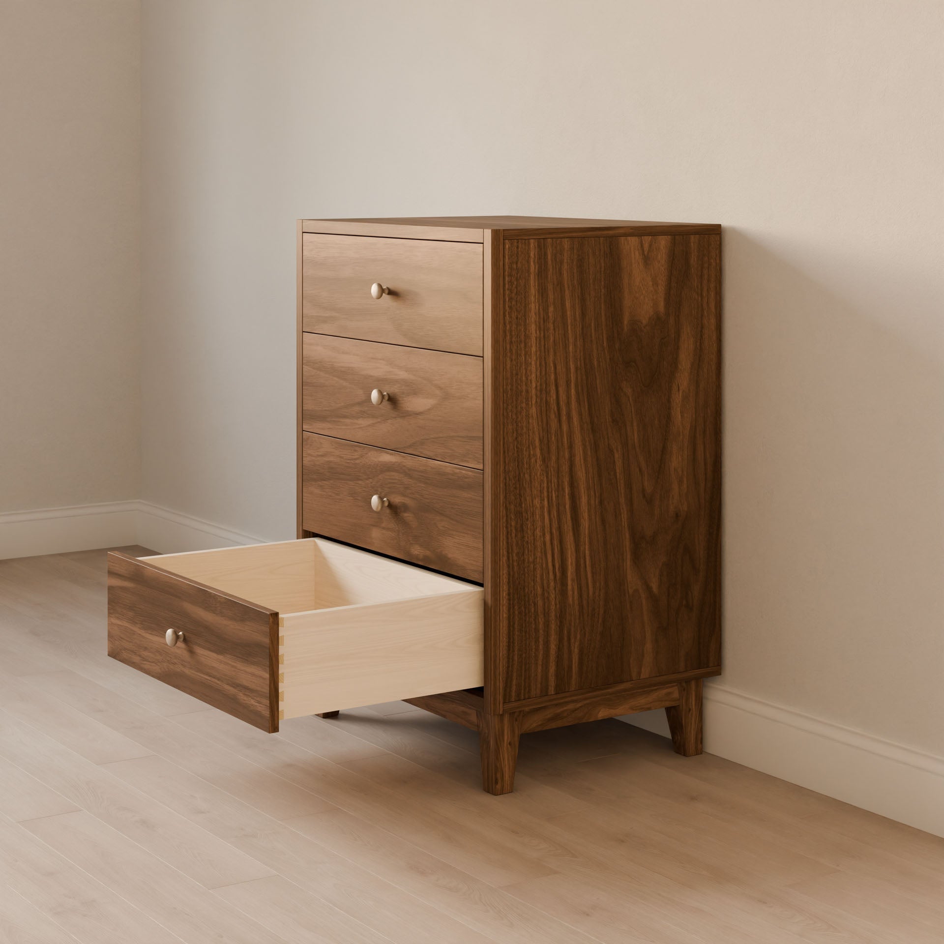 The Four Drawer Dresser in Walnut by Krovel Furniture Co. stands against a beige wall on a light hardwood floor. Crafted from premium cabinet grade plywood, its second drawer from the bottom is open, revealing a dovetailed solid Maple interior, while the others remain closed.