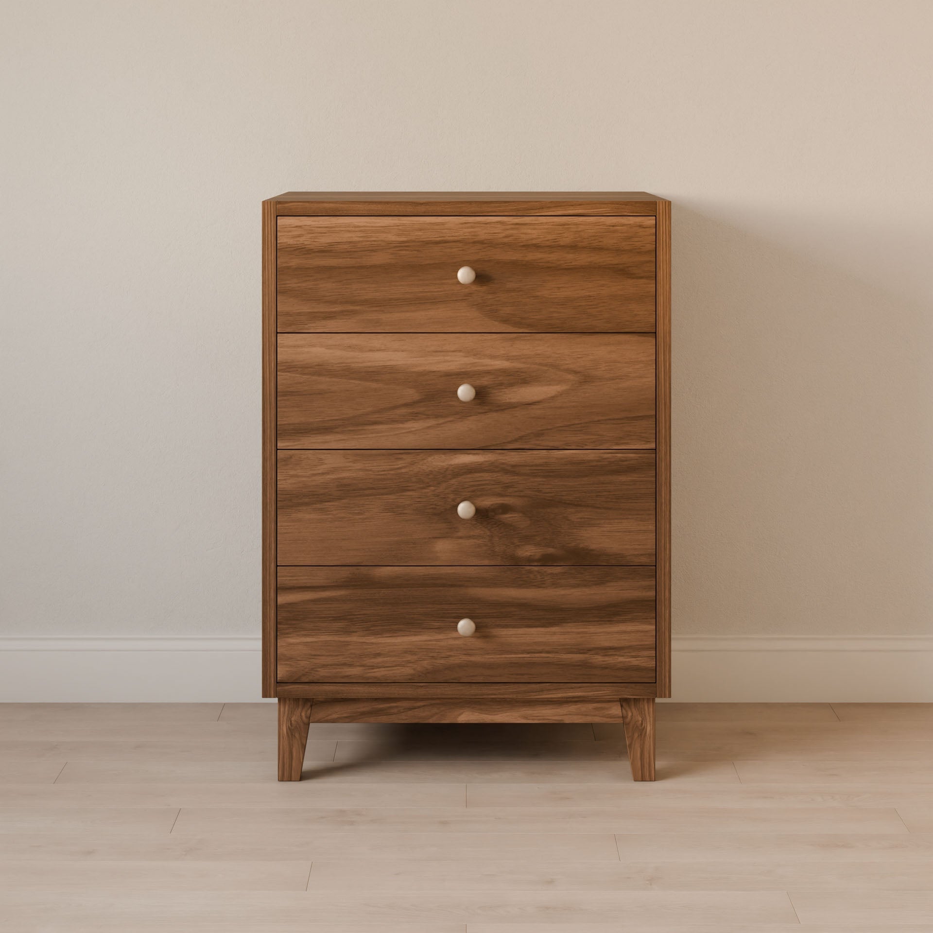 The Four Drawer Dresser in Walnut by Krovel Furniture Co., made from premium cabinet grade plywood with round white knobs, stands against a plain light-colored wall on a light wood floor.