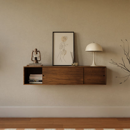 The Krovel Hardwood Oversized Media Console, set against a beige wall, displays a lamp, lantern, framed line art of a rose and person, diffuser, and books. On the floor to the right stands a vase with leafless branches.