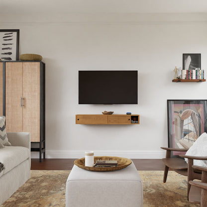 A modern living room features a wall-mounted TV above Krovel's Media Console Table in Cherry, finished in VOC-free polymerized linseed oil. A woven-design tall cabinet sits on the left, with a minimalist armchair and ottoman nearby, complemented by abstract art and books.