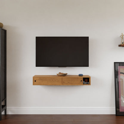 A wall-mounted TV above the Krovel Hardwood Media Console, topped with a bowl, round device, and electronics; minimalist decor includes framed artwork leaning on the floor to the right—perfect for a stylish media room.