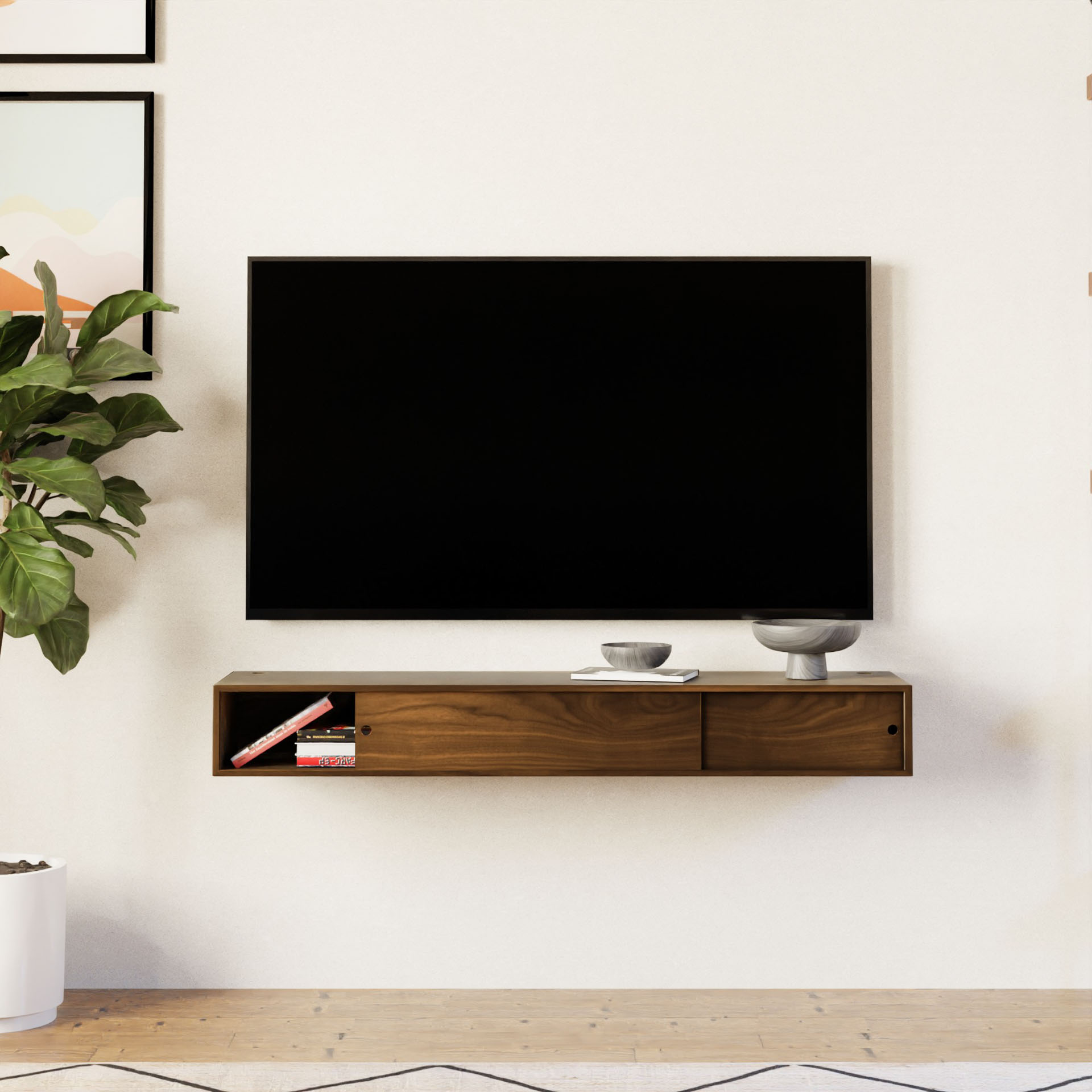 A modern living room features a wall-mounted flat-screen TV above a sleek Krovel Media Console Table in Walnut. The console holds books and two decorative bowls. To the left, a leafy plant stands by framed art, showcasing an American Cherry finish with a light, minimalistic design.