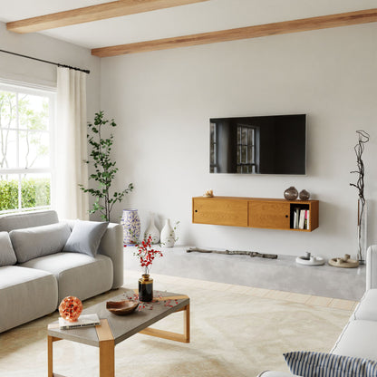 A modern living room with light gray sofas, a wooden coffee table, and the Krovel Hardwood Oversized Media Console beneath a wall-mounted TV. Decorative vases, lush plants, and large windows fill the space with natural light.