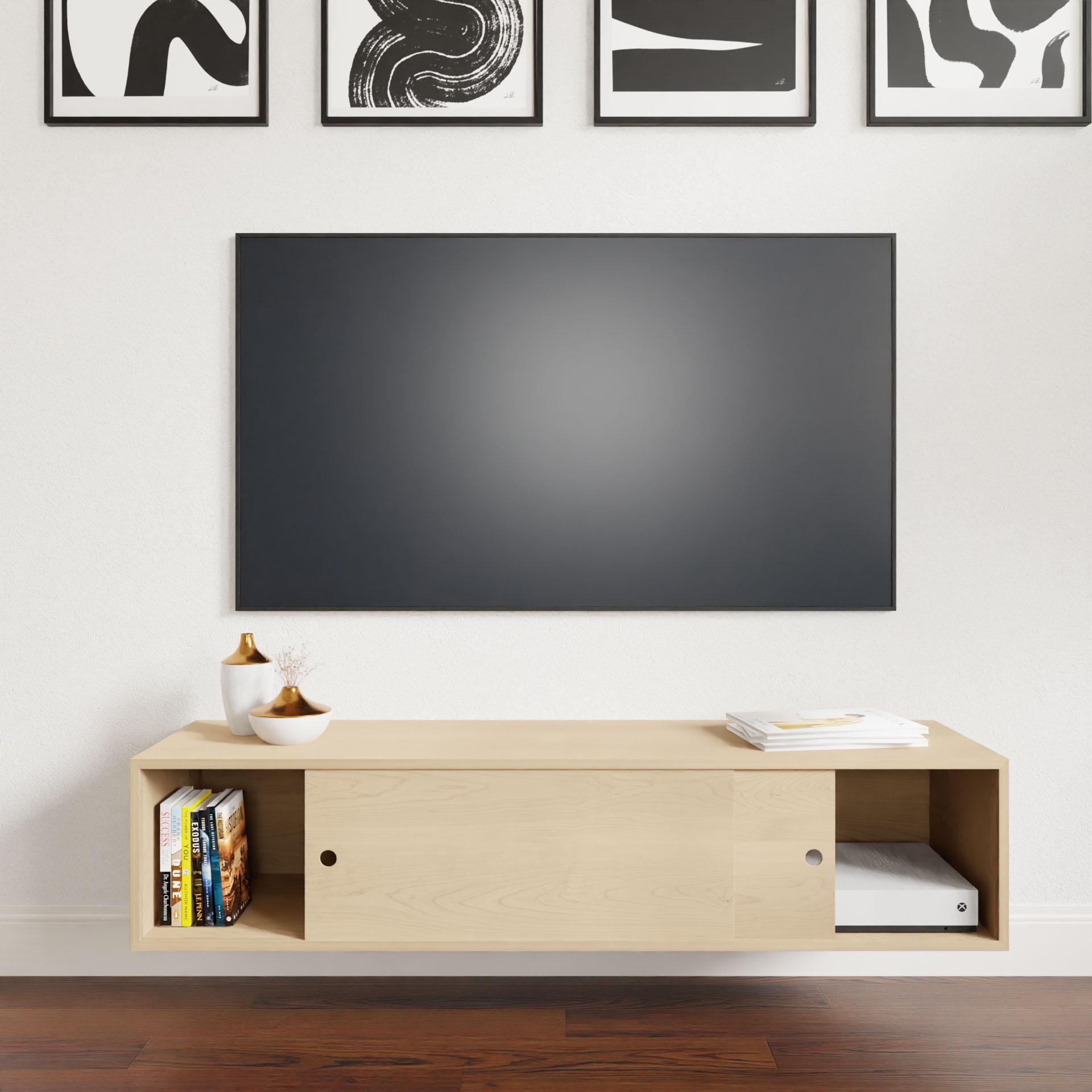 A minimalist living room features a wall-mounted flat-screen TV above an Oversized Media Console Table in Maple by Krovel. The cabinet holds books and decor. Four abstract black and white art pieces elegantly contrast with the dark wood floor, enhancing the room's aesthetic.