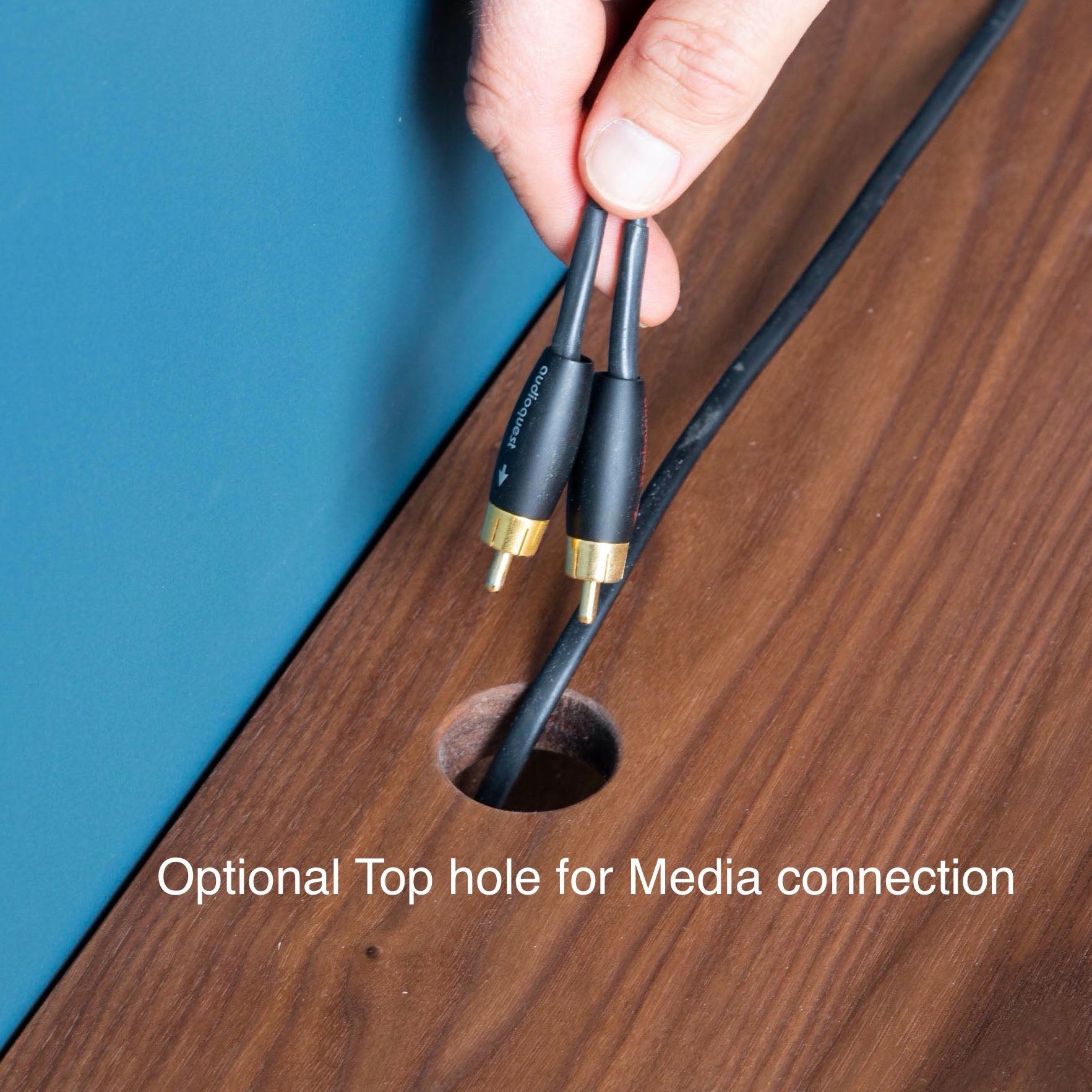 With a hand-finished touch, two audio cables featuring gold connectors are threaded through the "Optional Top hole for Media connection" on a walnut Oversized Media Console Table by Krovel, resting elegantly above a polished wooden surface.