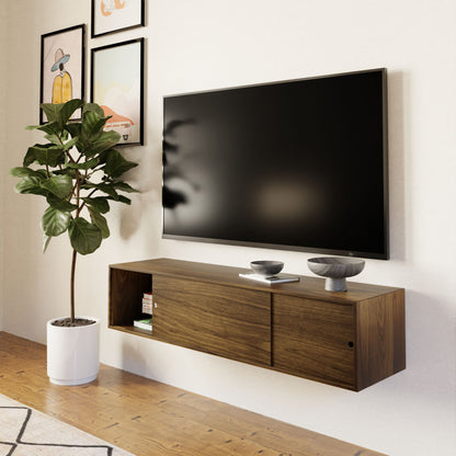 A modern living room with a wall-mounted flat-screen TV, the Krovel Hardwood Oversized Media Console, decorative bowls, a potted plant in a white pot, and framed art prints on a light-colored wall.