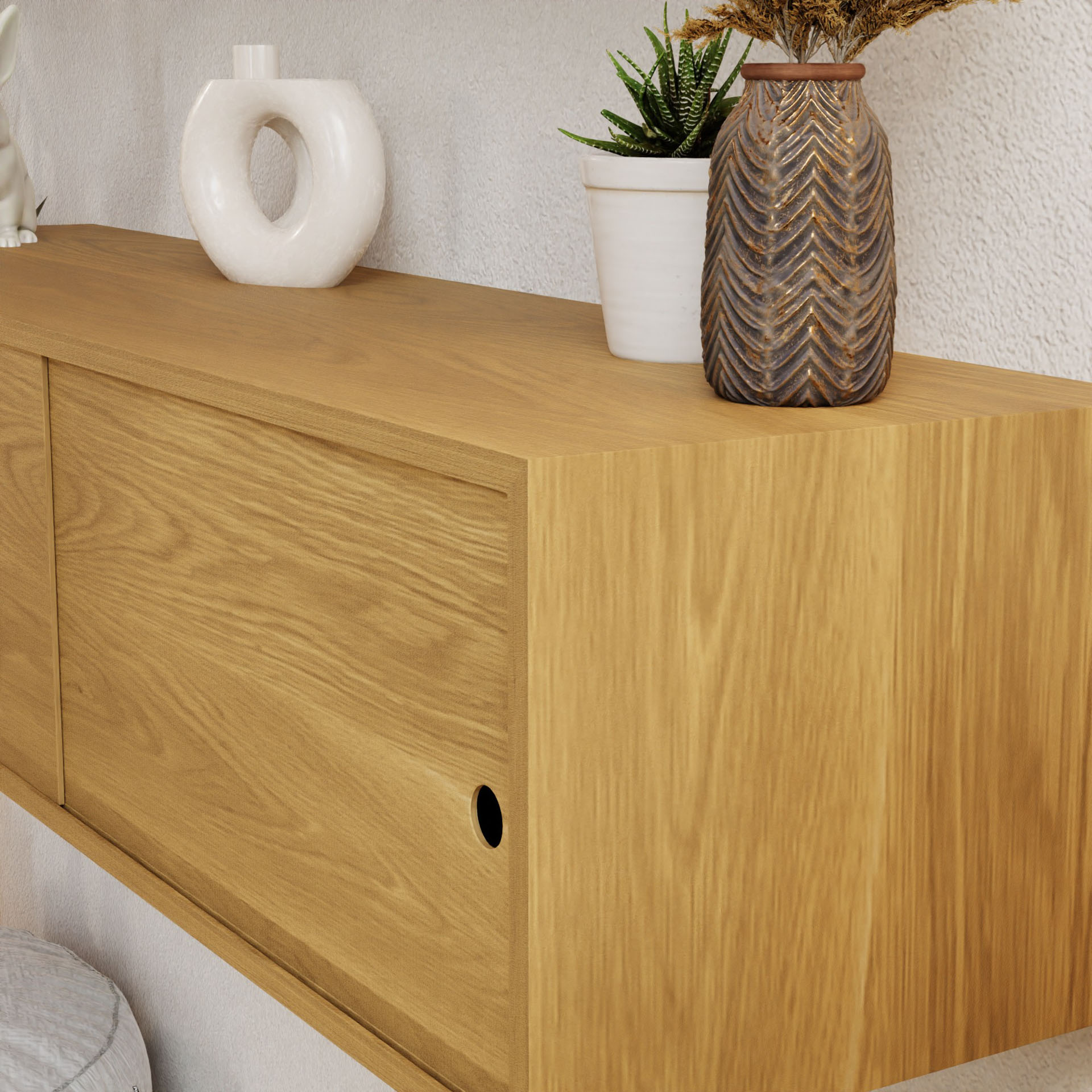 The Krovel Oversized Media Console Table in White Oak features a sliding door and has space for decorative items like a white circular vase, a small plant in a white pot, and a textured brown vase. It mounts easily against a light wall with French cleat mounting.
