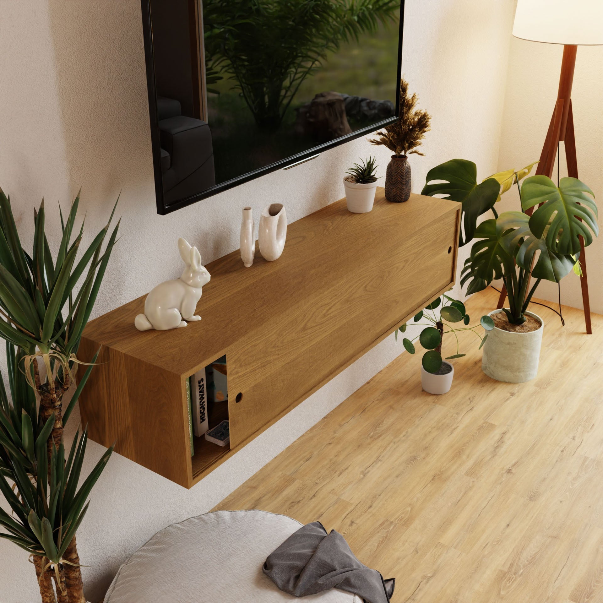 A modern living room features a wall-mounted wooden shelf of solid American cherry with decor like white vases and a bunny figurine. Potted plants adorn the area. A flat-screen TV using French cleat mounting is above, while a Krovel White Oak Oversized Media Console Table is below, and a standing lamp lights the corner.