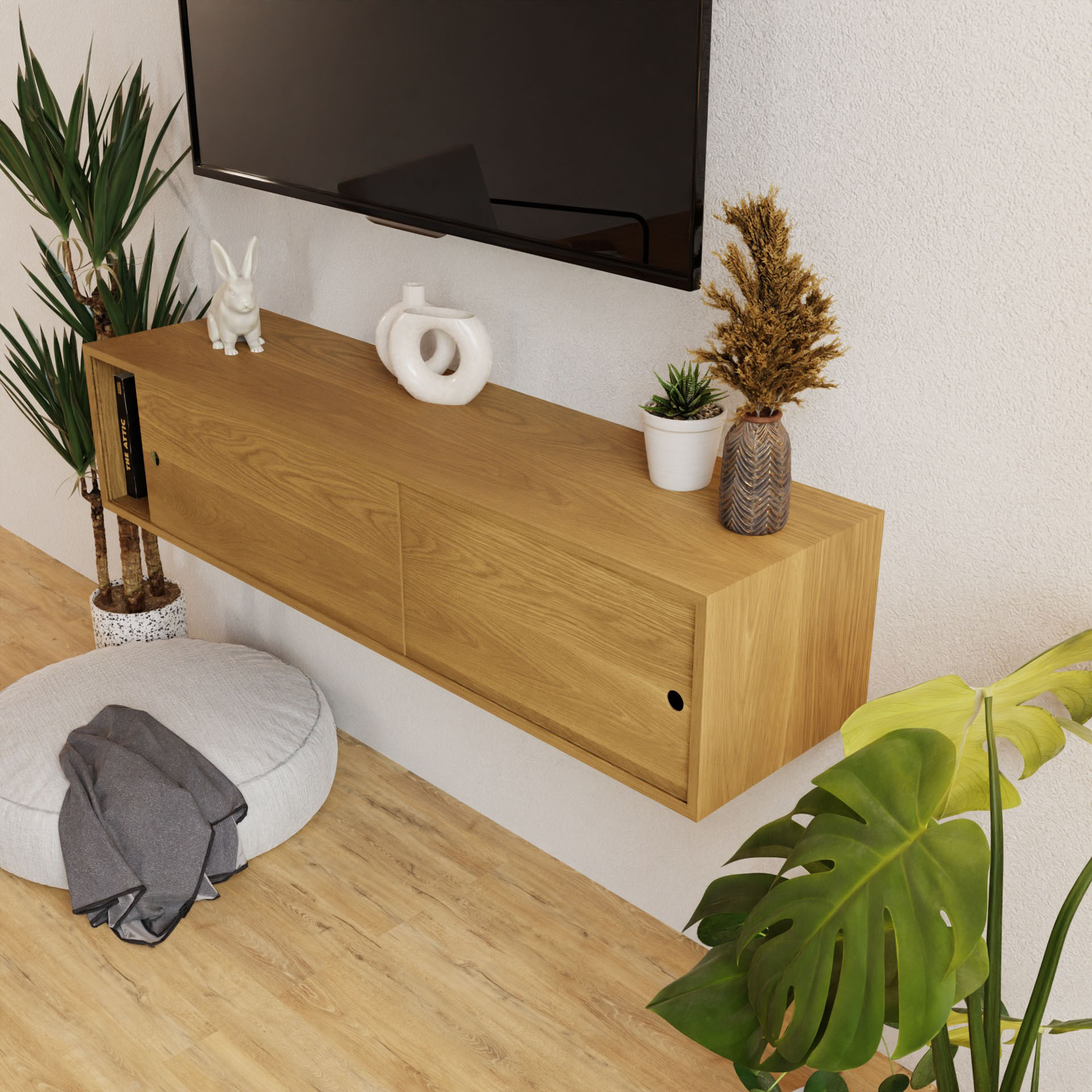 In a modern living room, a wall-mounted Krovel Oversized Media Console Table in White Oak adds elegance beneath a flat-screen TV. It is adorned with a white ceramic rabbit, circular sculpture, and vase of dried plants, complementing the large green plant by the round floor cushion.