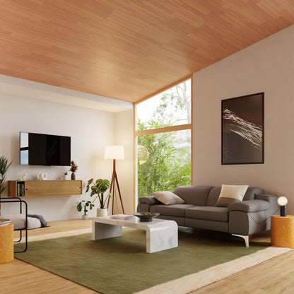 A modern living room showcases a gray sofa, white coffee table, and green rug. A flat-screen TV is elegantly mounted on a French cleat above an Oversized Media Console Table in White Oak by Krovel. Large windows offer lush views, enhanced by a tall floor lamp and solid American cherry wood accents.