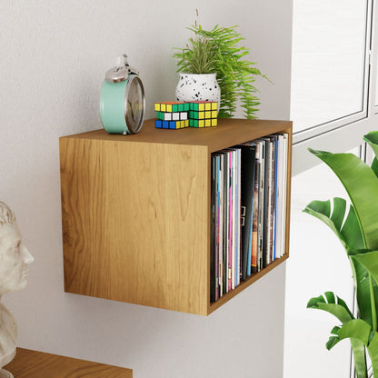 A Krovel Record Storage Shelf in Cherry, wall-mounted, displays vinyl records, a small plant in a white pot, a classic alarm clock, and two Rubik's cubes. Nearby are a window and large plant enhancing the mid-century modern vibe. Below the shelf peeks a bust sculpture.