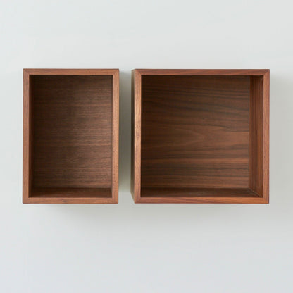 Two empty Krovel Hardwood Record Storage Shelves are mounted side by side on a light wall. Both have a smooth, dark solid hardwood finish—one is narrower and taller, the other is wider and shorter.