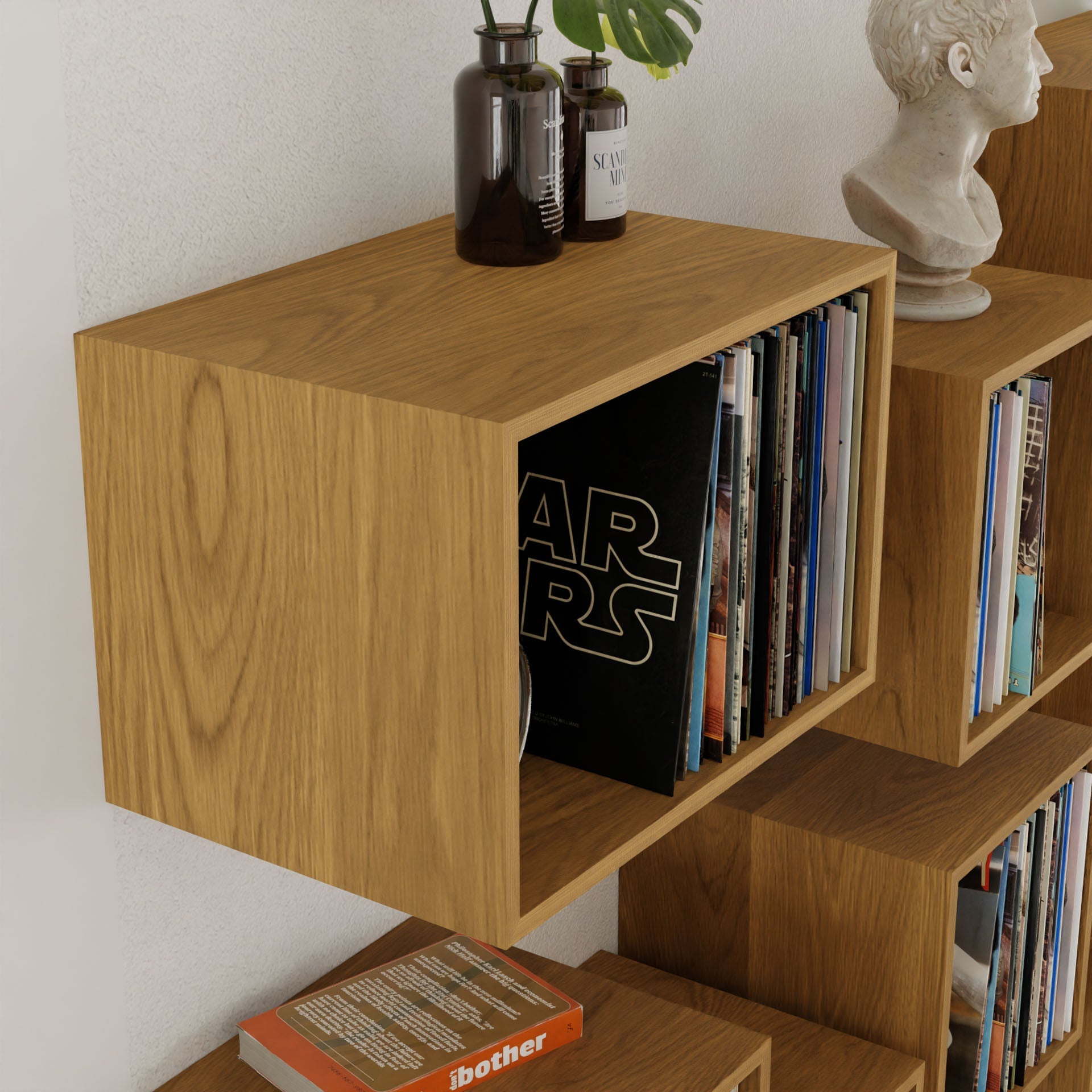 A wooden, mid-century modern bookshelf by krovel-dev holds books and magazines in its multiple sections. Among them is a "Star Wars" book, decorative vases, and a small white classical bust on top. Its American Black Walnut finish adds elegance to the room.