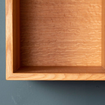 A close-up of a Record Storage Shelf in White Oak by krovel-dev against a dark green background. The shelf features smooth, polished surfaces with striking wood grain patterns, and the image highlights its expertly crafted corners and edges.