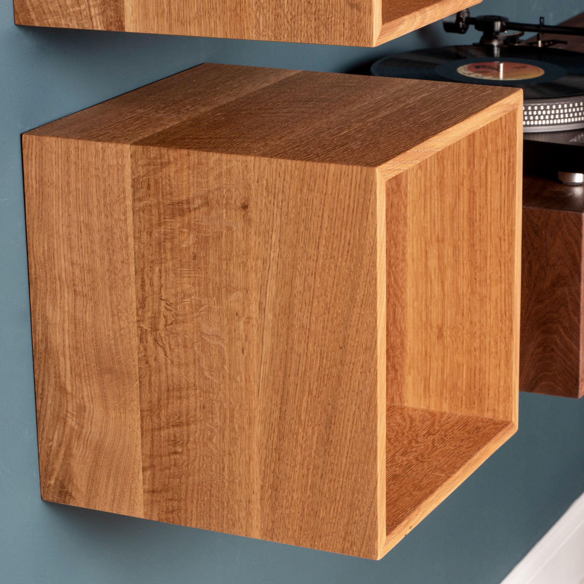 The krovel-dev Record Storage Shelves in White Oak are mounted on a blue wall, exuding a minimalist, mid-century modern vibe. A turntable is partially visible in the background, enhancing the retro flair of these floating shelves.