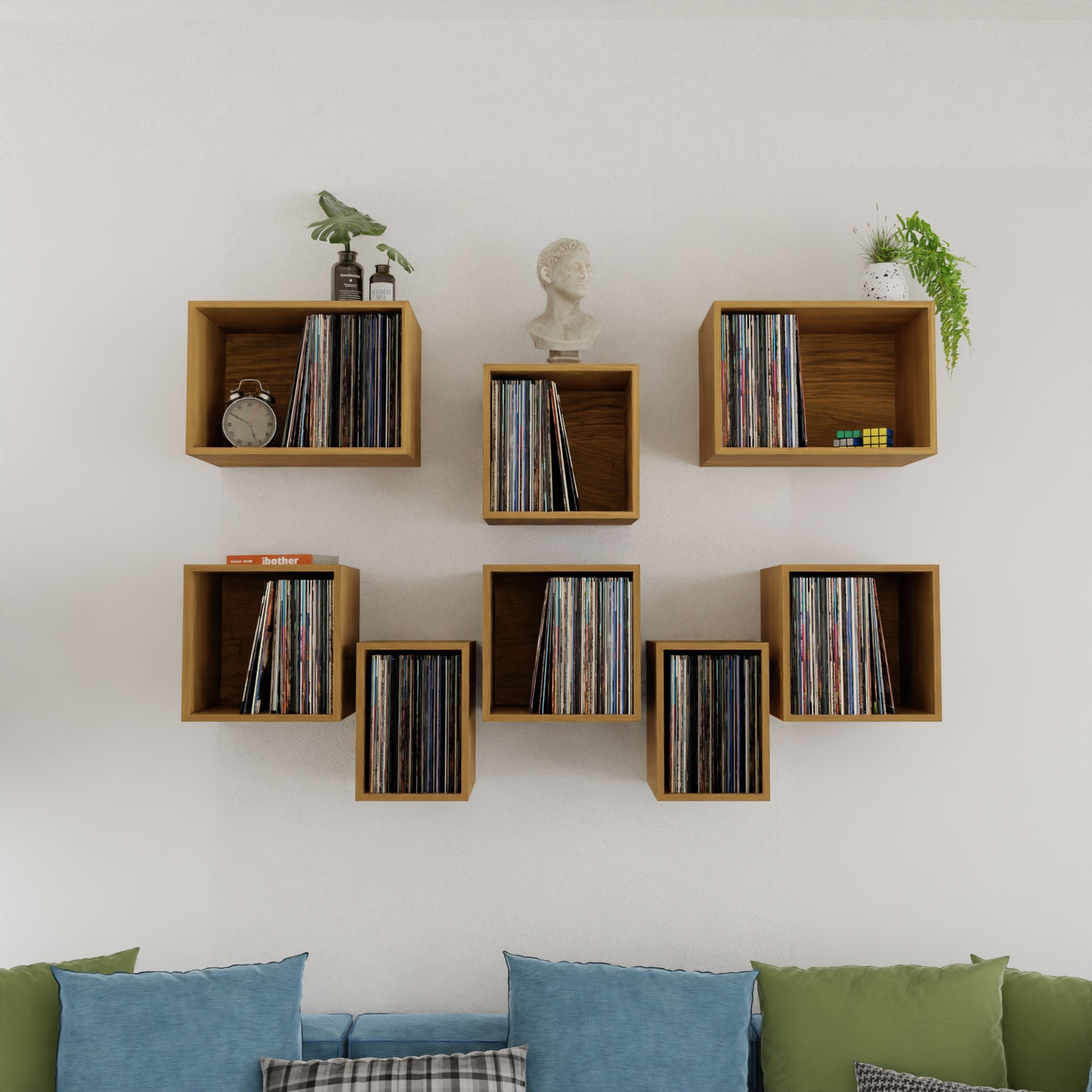 The Record Storage Shelves in White Oak by krovel-dev showcase vinyl records, a small bust, clock, plant, and Rubik's cubes above a cozy space featuring a blue and green cushioned sofa.