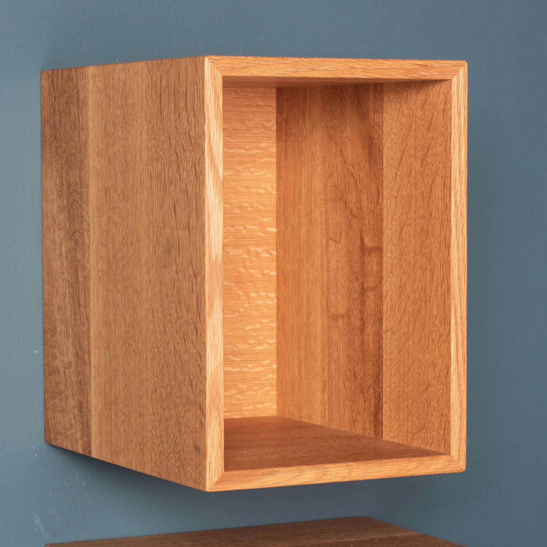 A mid-century modern wooden wall-mounted shelf by krovel-dev against a teal wall, featuring an open rectangular box design. This Record Storage Shelf in White Oak showcases the natural wood grain for a timeless aesthetic.