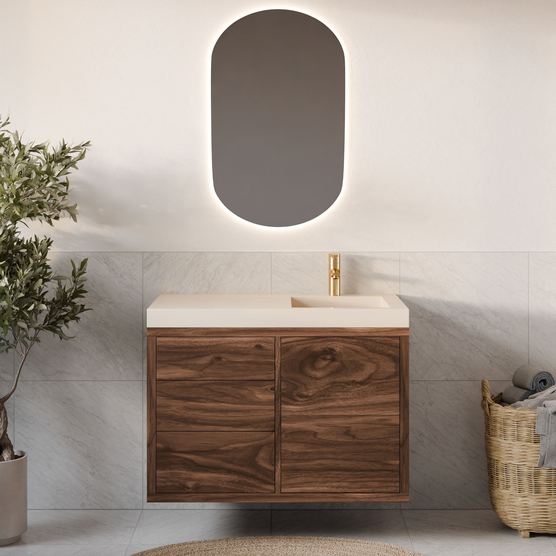 A modern bathroom highlights the Krovel Furniture Co. Single Door, Triple Drawer Vanity in Walnut with a white countertop and integrated sink. An oval backlit mirror hangs above, flanked by a potted plant and a woven basket of towels. Neutral tiles and soft-close hinges add elegance.#configuration_right-side-sink