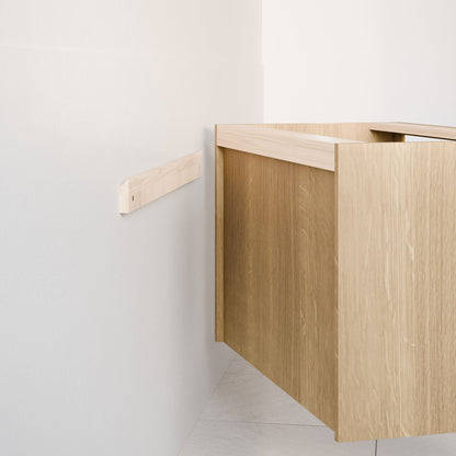 A Krovel Furniture Co. Maine Made Single Door, Triple Drawer Vanity in light wood is partially installed against a white wall, secured with a wooden mounting bracket. The room features light-colored tile flooring.