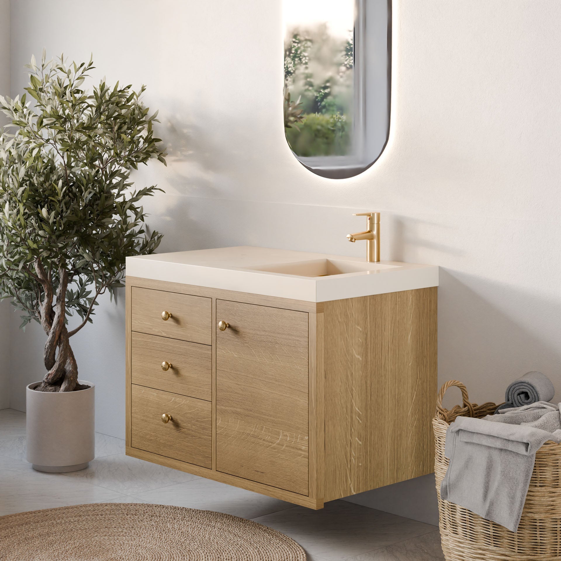 A modern bathroom features the Krovel Furniture Co. Maine Made Single Door, Triple Drawer Vanity in wood, paired with a gold faucet, oval mirror, potted plant, and basket of rolled towels in neutral tones and natural lighting.