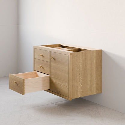 The Maine Made Single Door, Triple Drawer Vanity by Krovel Furniture Co. is a light wood floating sink vanity mounted on a white wall above pale floor tiles. It features one door and three drawers, with one drawer open to show empty space inside.