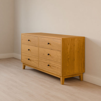 The Krovel Furniture Co. Six Drawer Dresser in Cherry, featuring black knobs and made from solid hardwood, complements a cream-colored wall on a light wood floor with its simple, modern design for a clean and minimalist look.