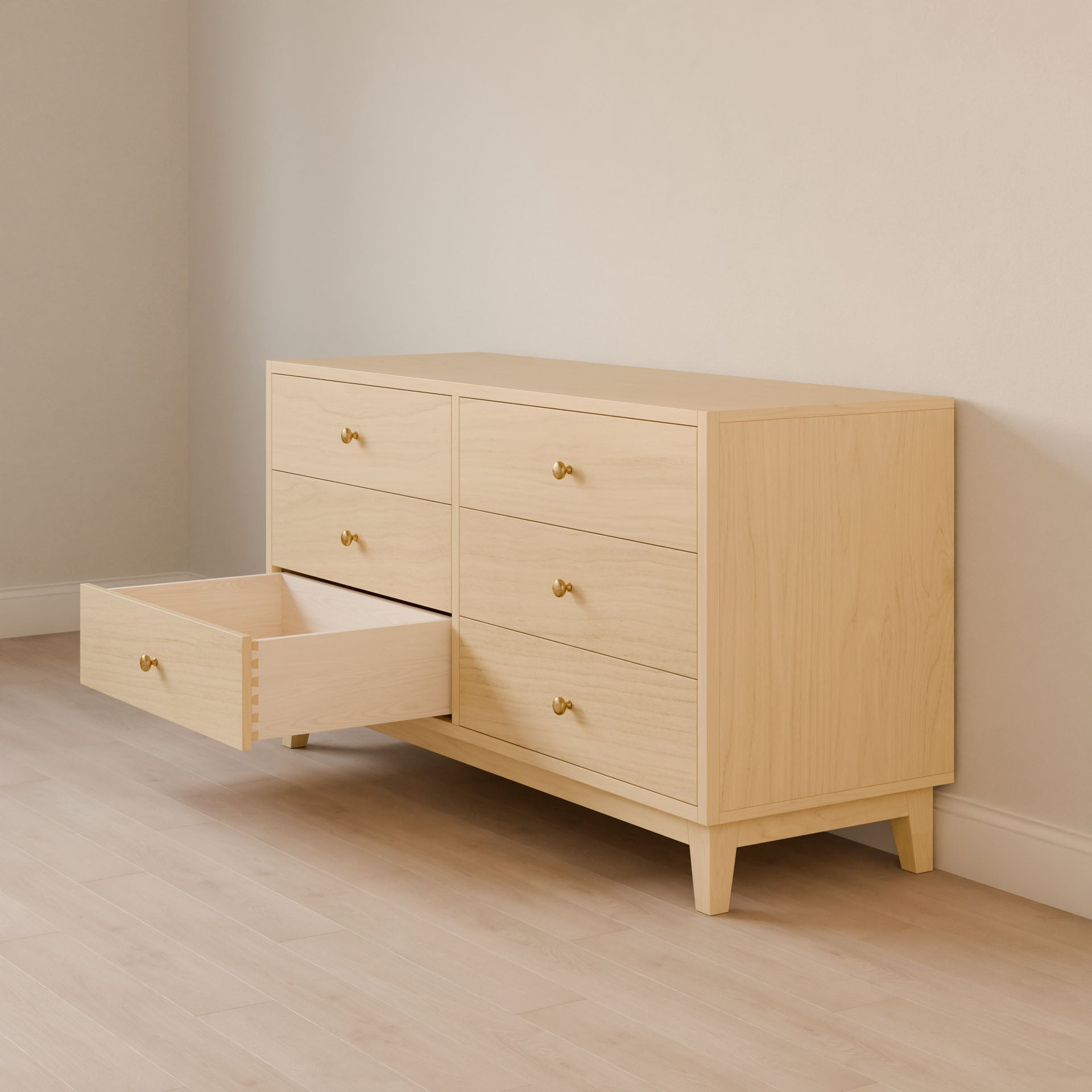 The Six Drawer Dresser in Maple by Krovel Furniture Co., made of premium plywood with sustainable construction, has six drawers (three on each side) with small round golden knobs. It sits on short legs in a room with light timber flooring and neutral walls, with one left drawer partially open.