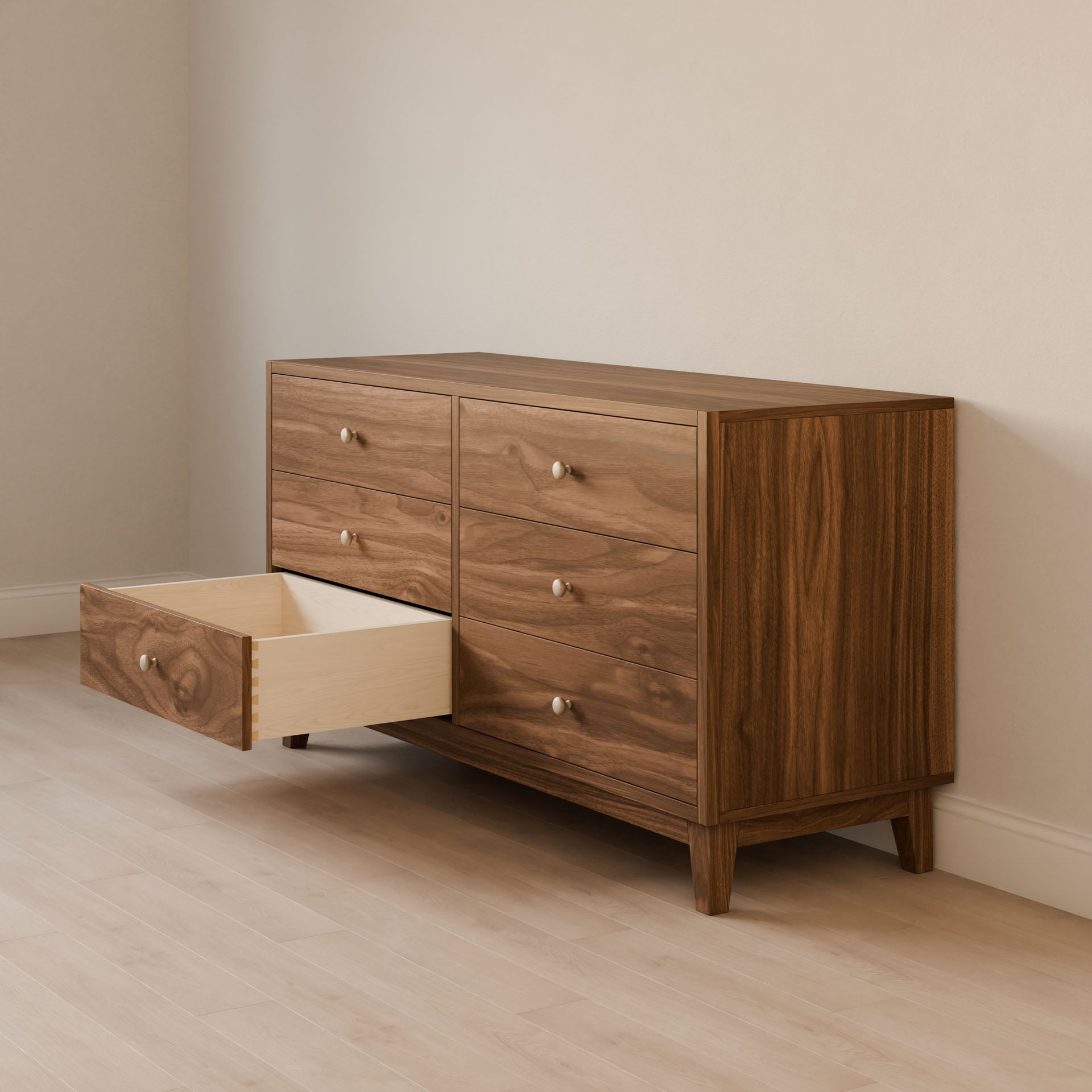 The Maine Made Six Drawer Dresser by Krovel Furniture Co. stands against a light wall on a pale wood floor, with one left drawer open to show its light interior. This solid wood veneer cabinet is handmade in Portland, Maine.