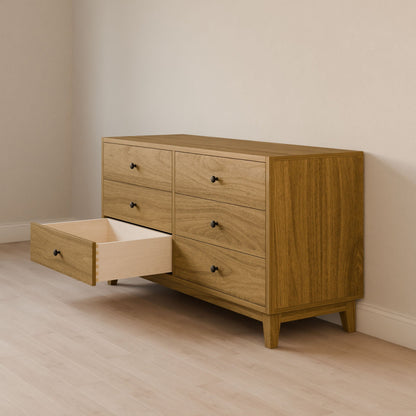 The Six Drawer Dresser in White Oak from Krovel Furniture Co. stands on light wood flooring against beige walls. One middle drawer is open, showing an empty space. Crafted from solid hardwood, it features simple black knobs and sustainable construction with formaldehyde-free plywood.
