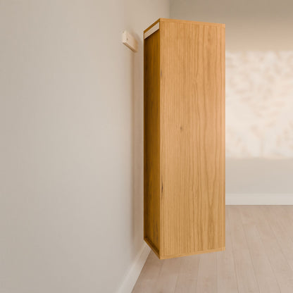 In a minimalist room with light wood flooring, the Triple Drawer Linen Cabinet in Cherry by Krovel Furniture Co. is elegantly mounted sideways on the wall. Its vertical alignment creates intriguing light and shadow patterns, embodying sustainable principles while adding airy elegance to the space.