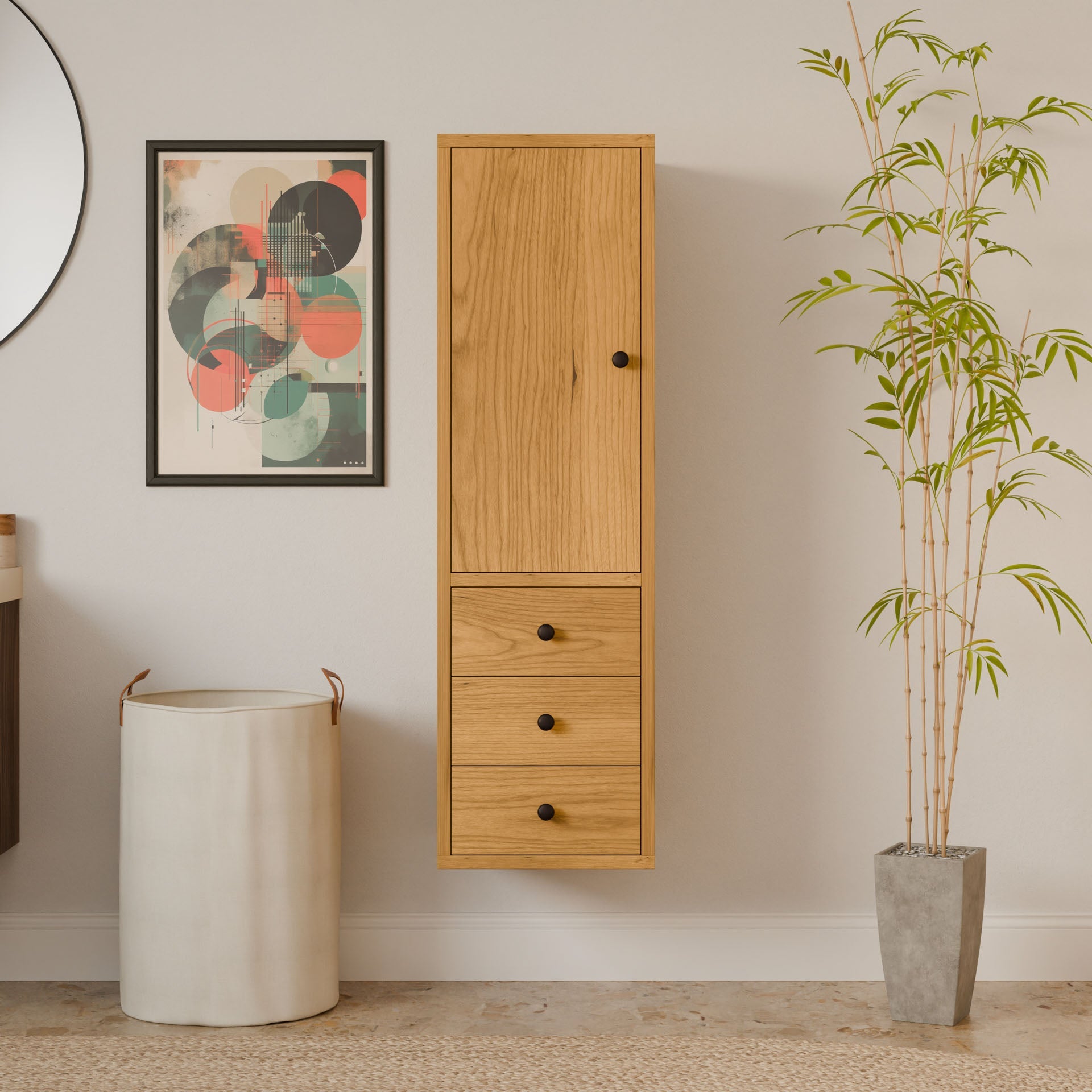 A minimalist interior features Krovel Furniture Co.s Triple Drawer Linen Cabinet in Cherry, emulating bathroom vanity style with three drawers and a tall door. A round mirror is partially visible on the left, abstract art decorates the wall, and a tall plant in a square pot stands on the right.