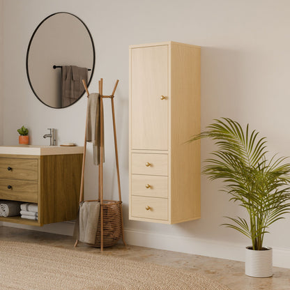 A minimalist bathroom features light wood fixtures and a hardwood face frame. Above the sink hangs a round mirror, next to Krovel Furniture Co.s Triple Drawer Linen Cabinet in Maple. A towel rack stands near a potted plant on tiled flooring, with a textured rug completing the serene space.