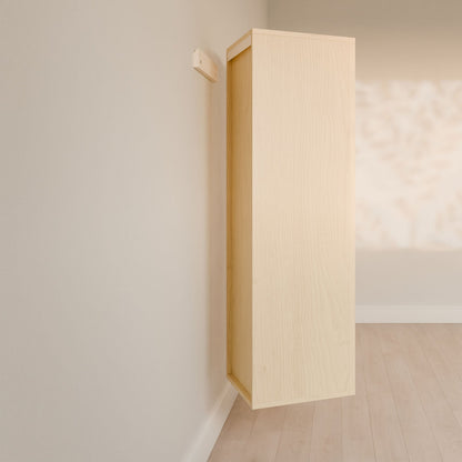 The Triple Drawer Linen Cabinet in Maple by Krovel Furniture Co. appears to float against a pale wall, casting shadows of leaves. Its open design with elegant hardwood face frames is complemented by light wood flooring, adding warmth to the minimalist setting.