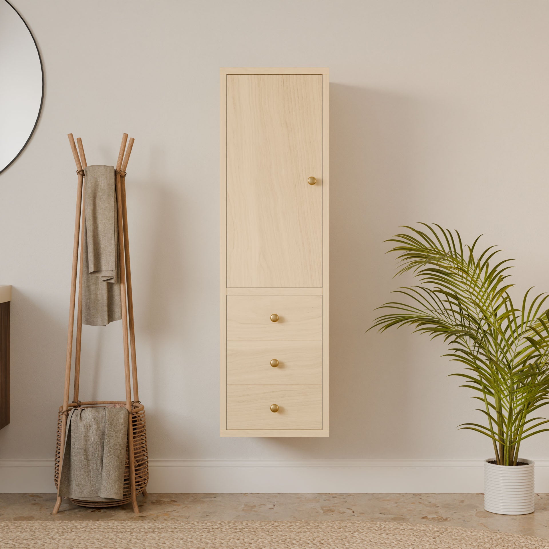 A minimalist interior showcases the Triple Drawer Linen Cabinet in Maple by Krovel Furniture Co., featuring soft-close drawers and a hardwood face frame against a neutral wall. A round mirror, tall coat rack with a towel and basket, and a potted plant complement the decor, illuminated by natural light for serenity.