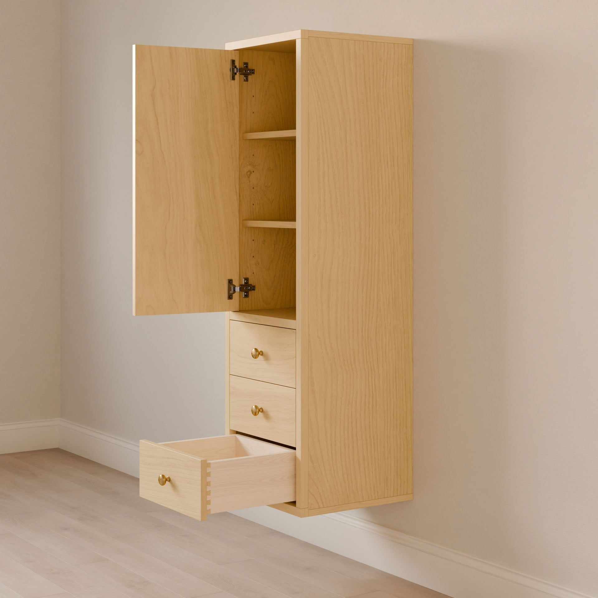 The Triple Drawer Linen Cabinet in Maple by Krovel Furniture Co. is showcased with an open door revealing two shelves, and a slightly pulled-out soft-close drawer. It features brass knobs and a hardwood face frame, set against a light-colored wall and light wood flooring.