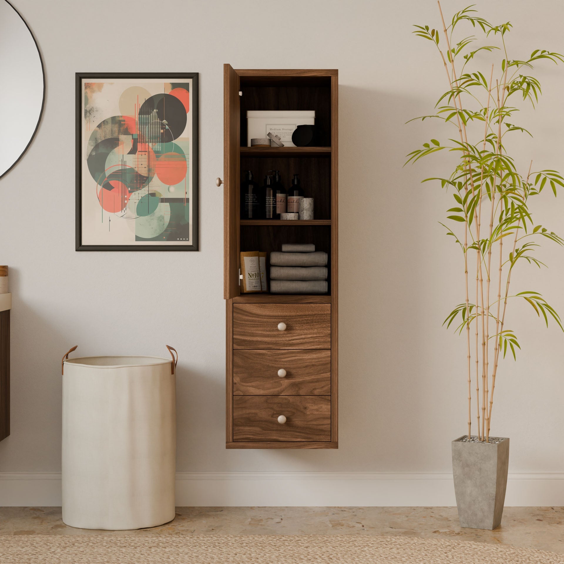 In a minimalist bathroom, the open Triple Drawer Linen Cabinet in Walnut by Krovel Furniture Co. displays towels and toiletries. A colorful geometric art piece and a round mirror add flair, while a tall plant and laundry basket on the floor embody sustainable design elements.