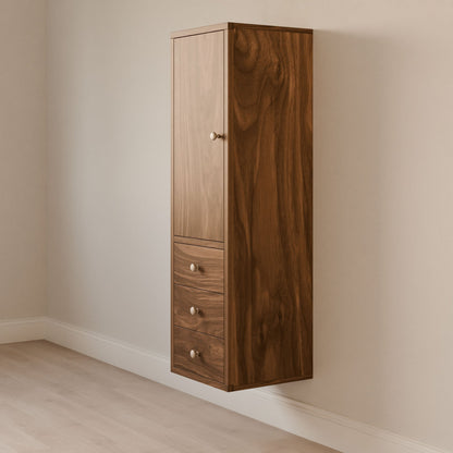 The Krovel Furniture Co.s Triple Drawer Linen Cabinet in Walnut is a wall-mounted, rectangular wooden cabinet made from solid hardwood. It features a door on the upper section and three drawers with round metal knobs below, set against a light-colored wall and floor.