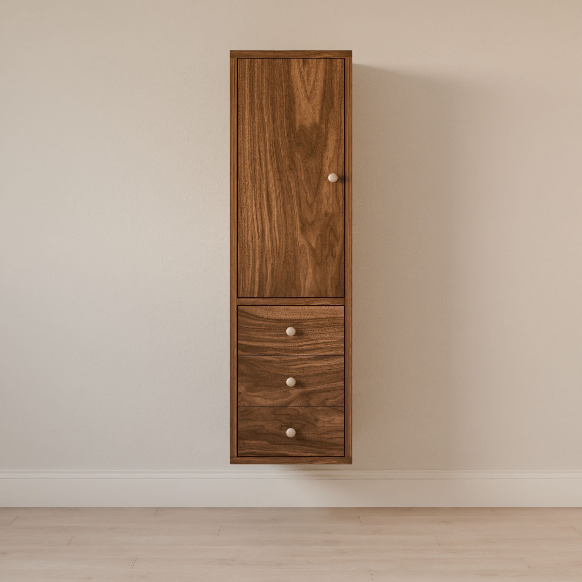 The Triple Drawer Linen Cabinet in Walnut by Krovel Furniture Co. is a tall, solid hardwood cabinet with a light brown finish, mounted on a beige wall. It has one top door and three lower drawers with round knobs, crafted using sustainable techniques and casting a shadow over the light wood floor below.