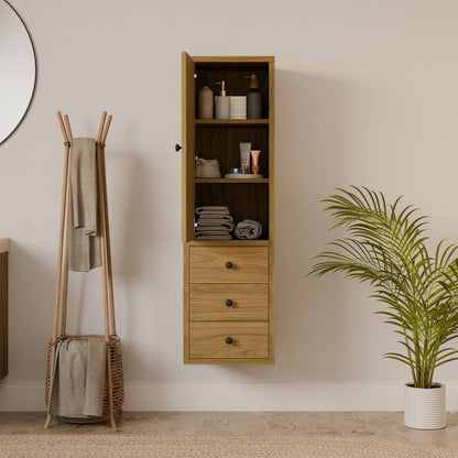 The Triple Drawer Linen Cabinet in White Oak by Krovel Furniture Co. has a hardwood face frame and open shelving for toiletries and towels. It complements a round mirror, towel rack with linens, and potted plant on the tiled floor.